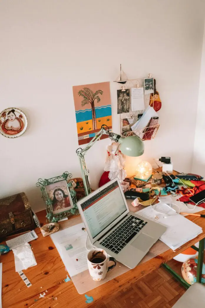 Cozy home workspace with a laptop, coffee mug, desk lamp, notes, and creative decor on a wooden desk.